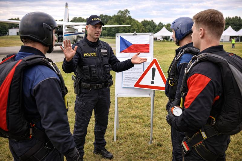 Předletová příprava parašutistů s policistou na travnaté ploše letiště u bílého letadla