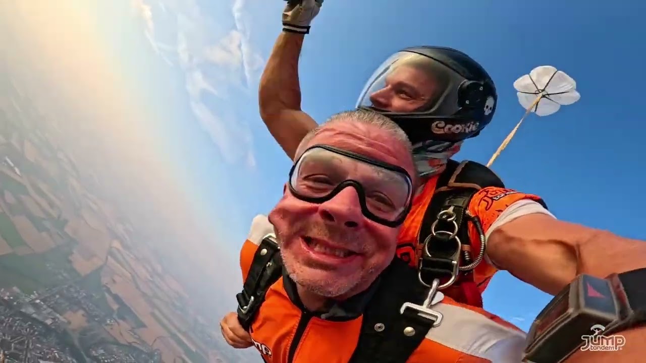 Náhled videa ze selfie kamery: usmívající se pasažér v brýlích a tandem pilot v černé helmě ve volném pádu