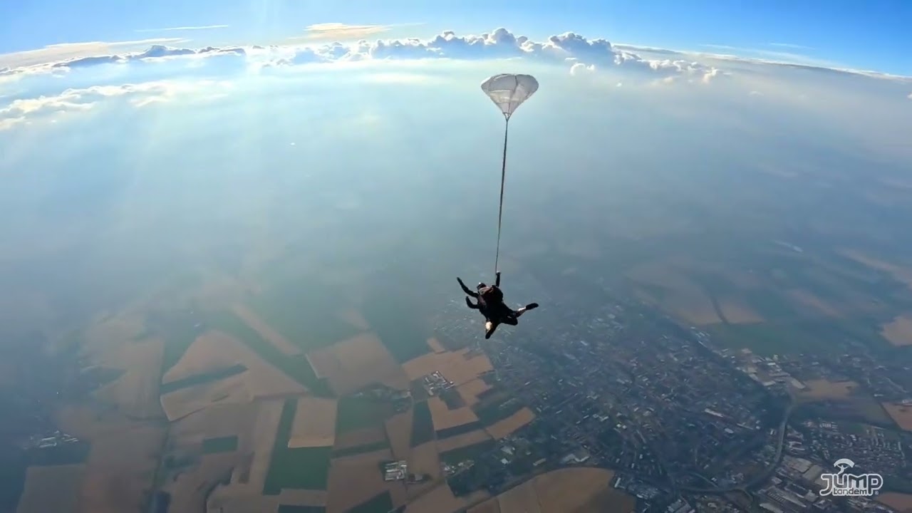 Náhled videa z externí kamery: tandem se stabilizačním padáčkem ve volném pádu nad poli a městem